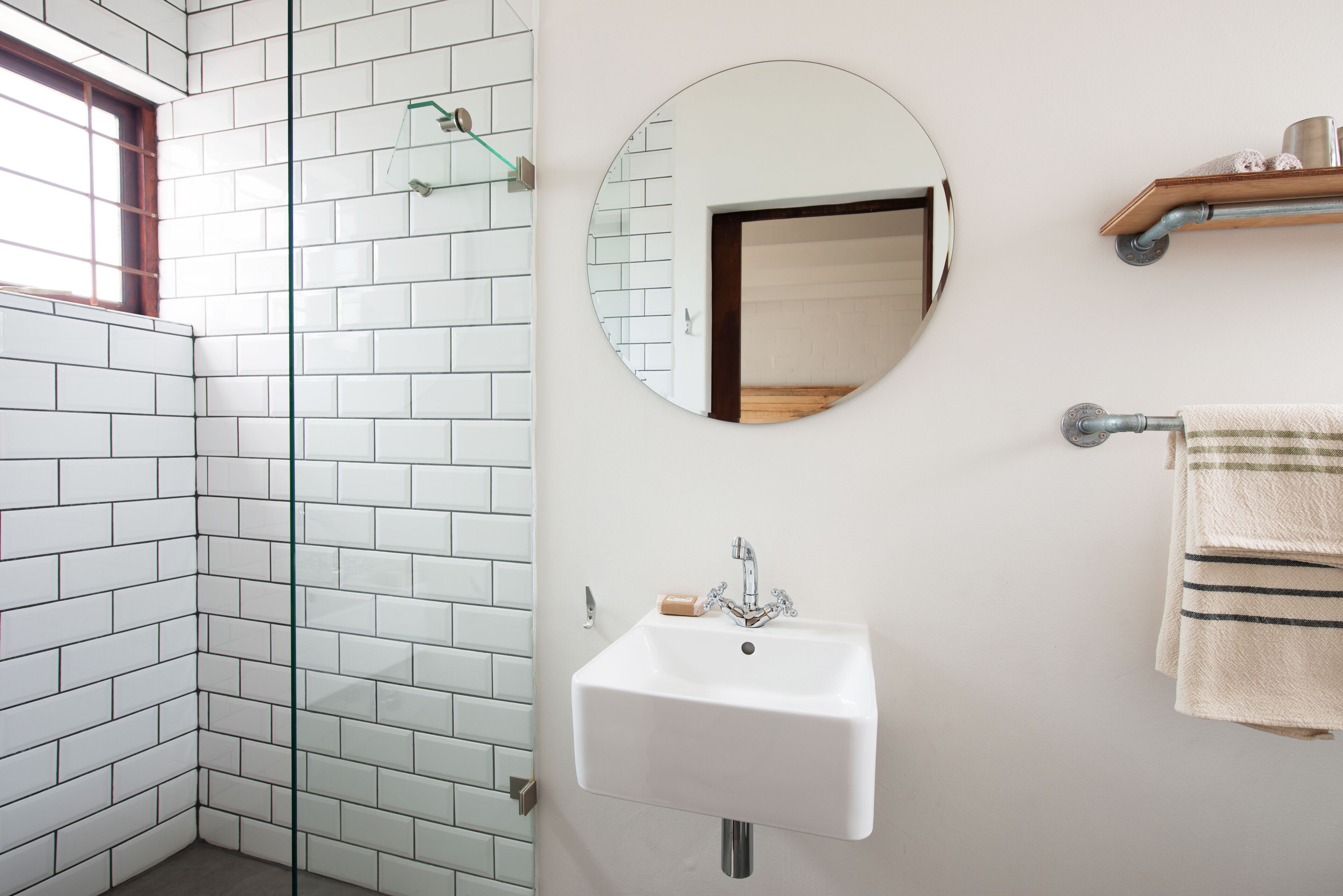Un baño con paredes de azulejos blancos, un lavabo blanco, un espejo redondo y un perchero para toallas.