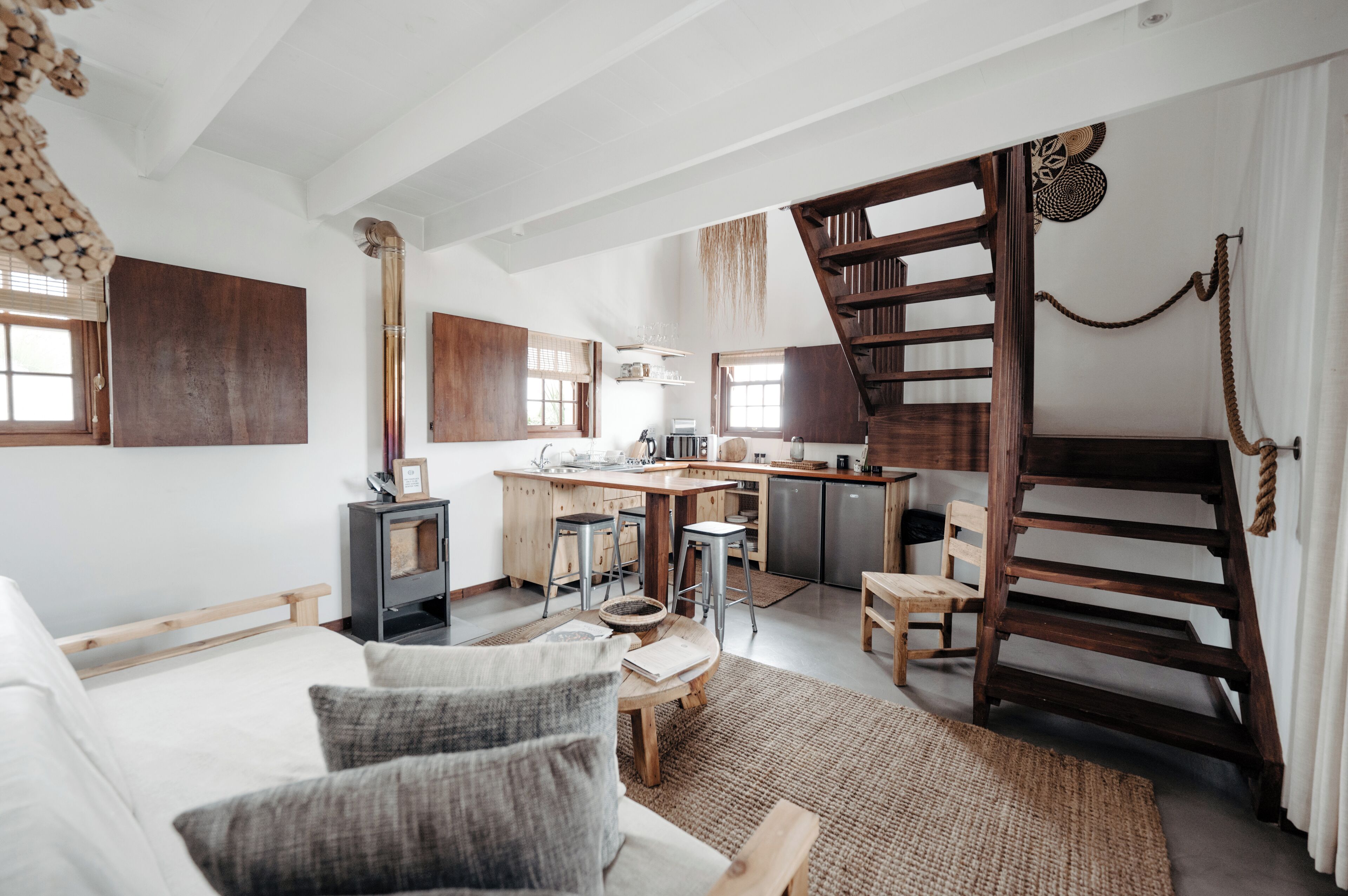 A spacious living area with a large sofa, a wooden staircase, and a kitchen area with a wooden island and bar stools.