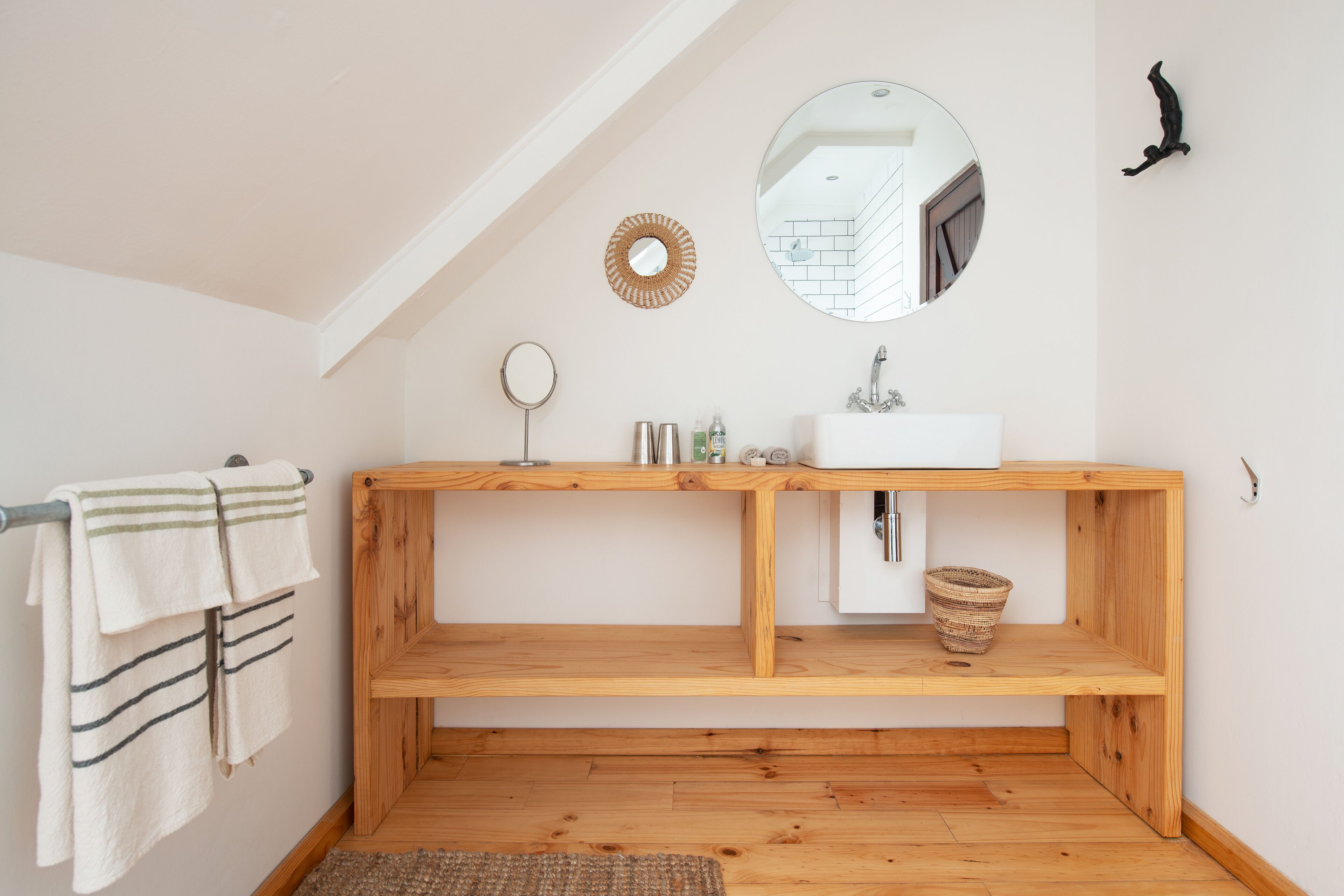 Een badkamer met een houten wastafelmeubel, een ronde spiegel, een wastafel en een handdoekhouder.