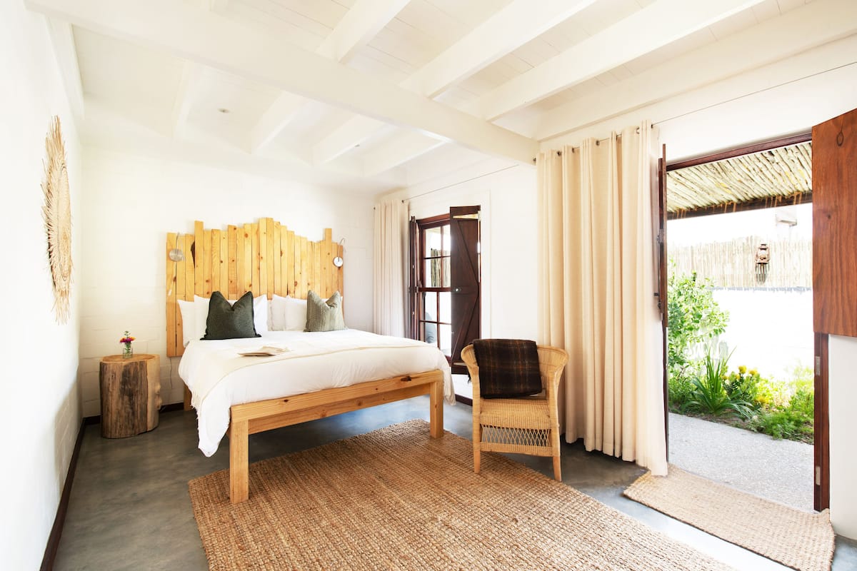 A bedroom with a wooden bed, a wicker chair, and a large window with curtains.