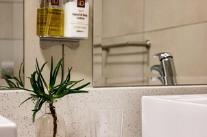 A bathroom with a hand and body lotion dispenser, a glass, and a plant on the counter.