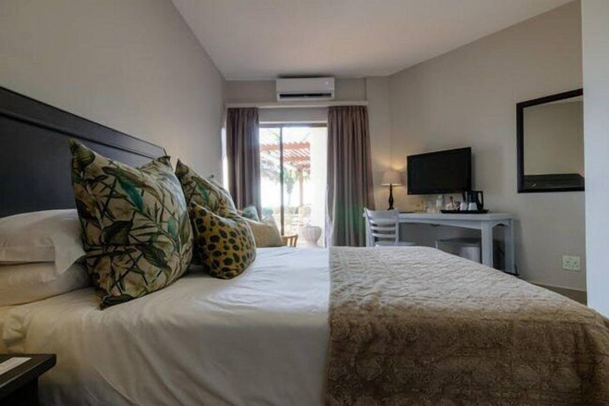 A hotel room with a bed, a desk with a flat-screen TV, and a window with curtains.