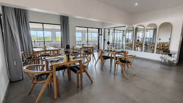 A spacious dining area with multiple tables and chairs, large windows, and a view of the outdoors.