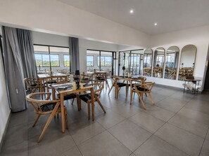 A spacious dining area with multiple tables and chairs, large windows, and a view of the outdoors. - The Ridge Guesthouse (Richards Bay)