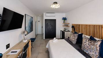 Habitación de hotel con cama, escritorio con silla, televisor de pantalla plana, un cuadro, lámpara del techo y una puerta.