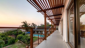A covered balcony with a view of a swimming pool and lush greenery. - The Ridge Guesthouse (Richards Bay)
