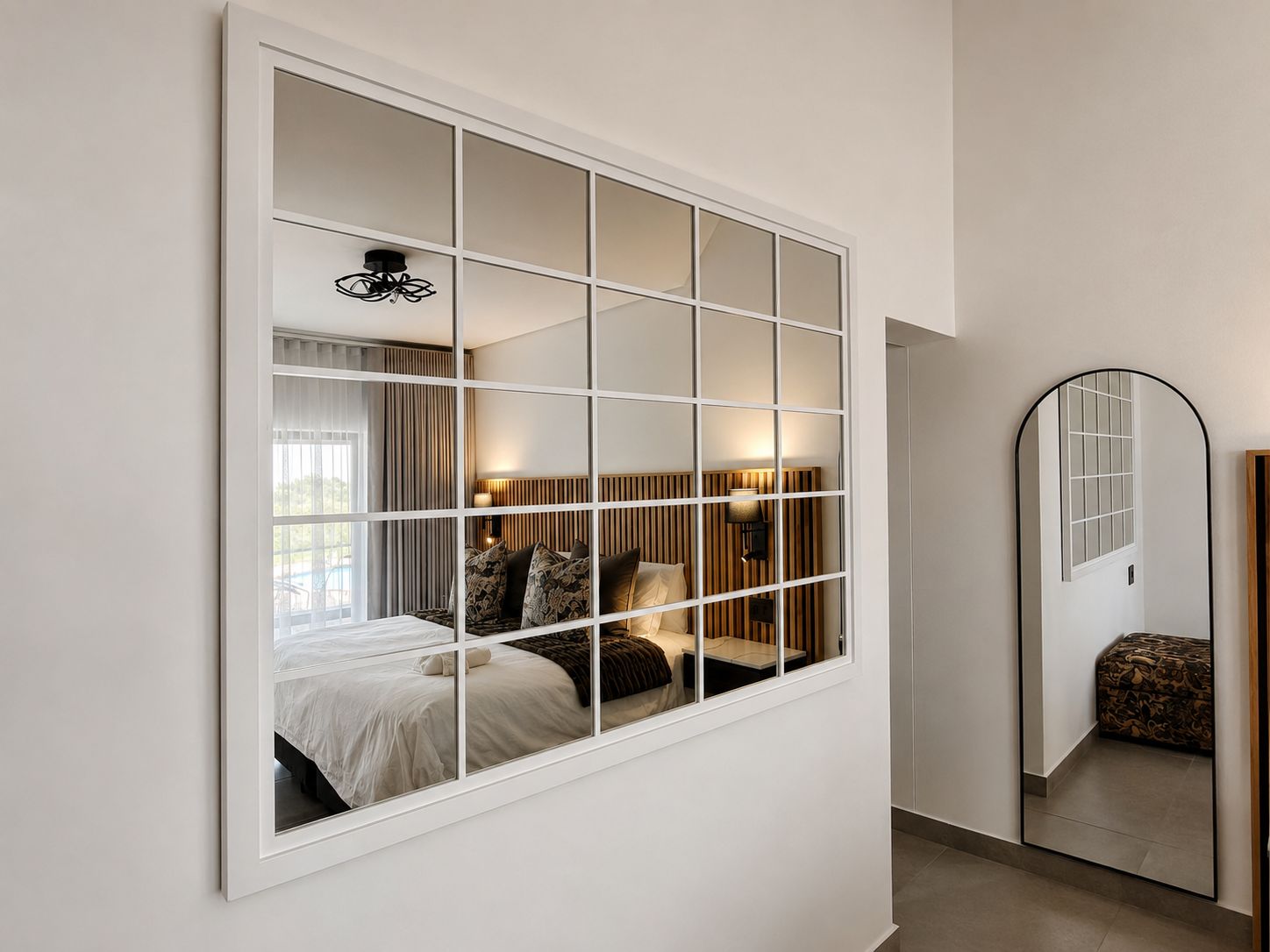 A bedroom with a large window, a bed, a bedside table, a lamp, and a mirror.