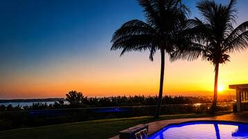 A swimming pool with a sunset view, palm trees, and a distant shoreline.