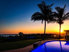 A swimming pool with a sunset view, palm trees, and a distant shoreline. - The Ridge Guesthouse (Richards Bay)