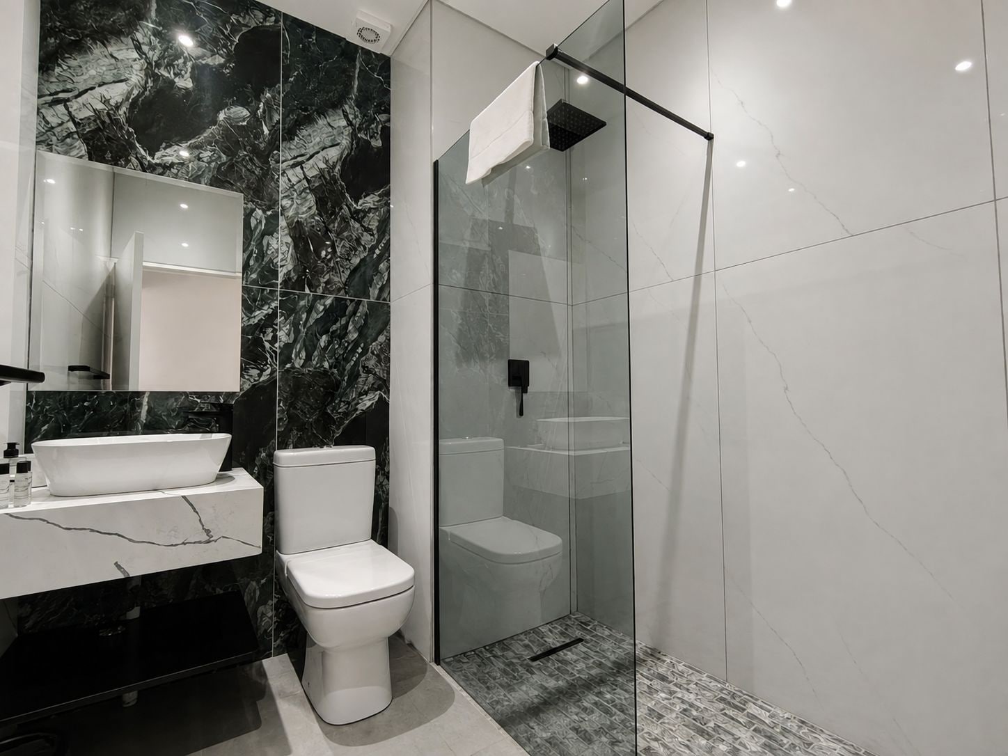 A modern bathroom with a marble backsplash, a freestanding toilet, a glass-enclosed shower, and a vanity with a sink.