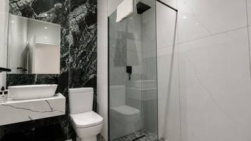 Un baño moderno con salpicadero de mármol, inodoro independiente, ducha con mampara de vidrio y tocador con lavabo.