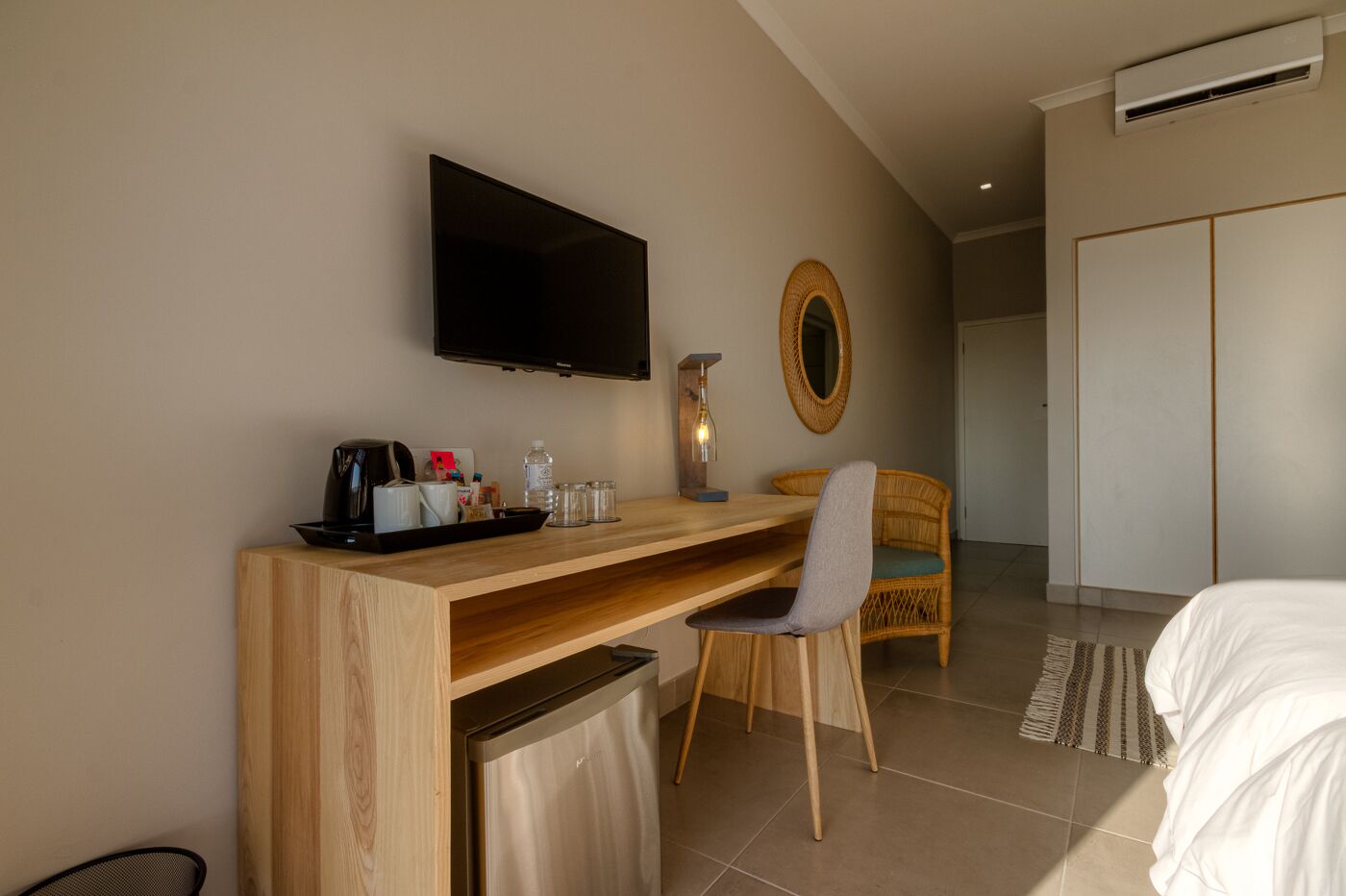 Una habitación de hotel con un escritorio de madera, televisor, una silla de mimbre, una cama y un armario.
