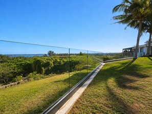 A modern house with a glass railing overlooking a grassy area and a body of water. - The Ridge Guesthouse (Richards Bay)