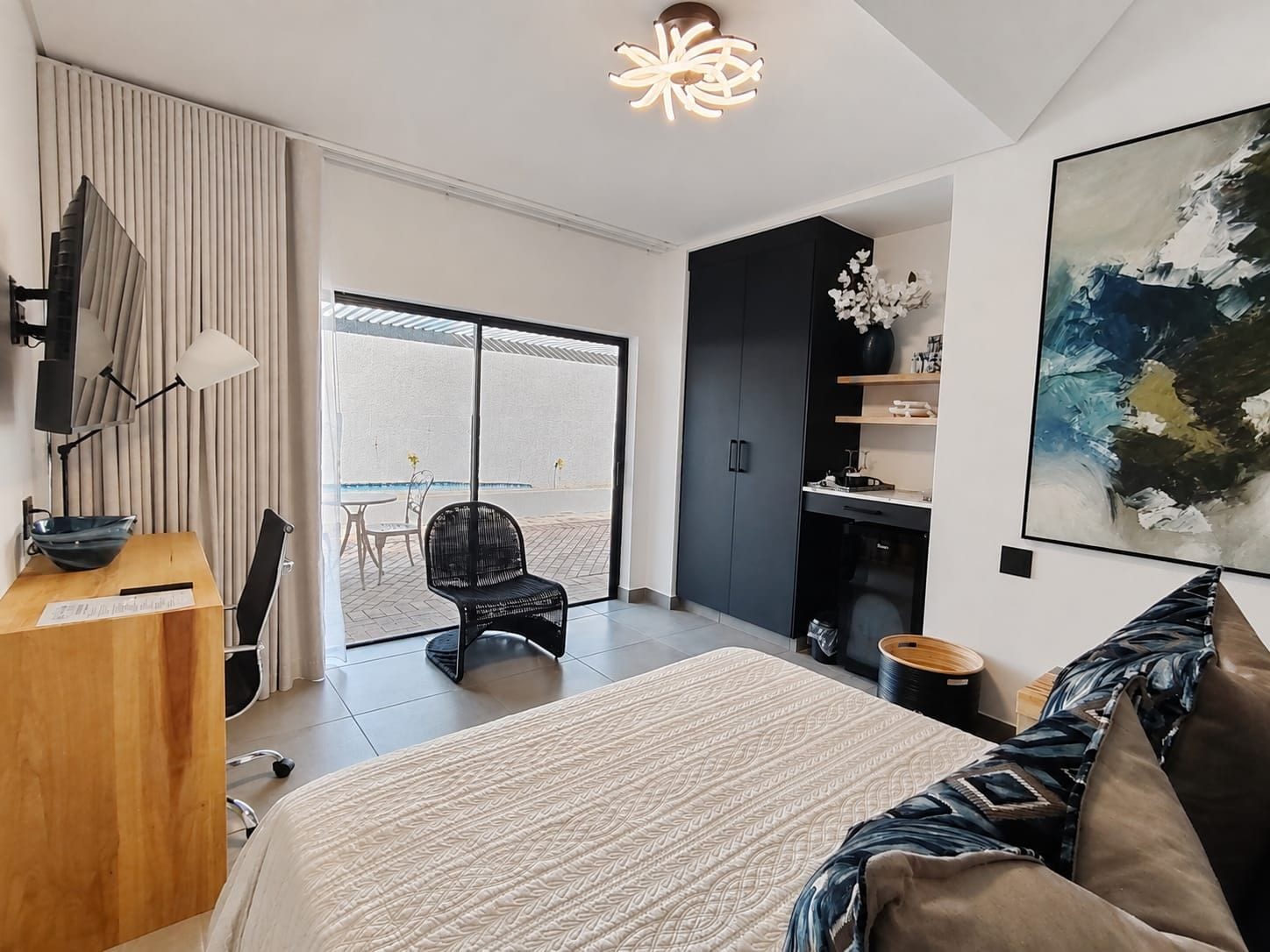 Ein modernes Schlafzimmer mit einem großen Bett, einem Schreibtisch, einem Stuhl und Blick ins Freie.
