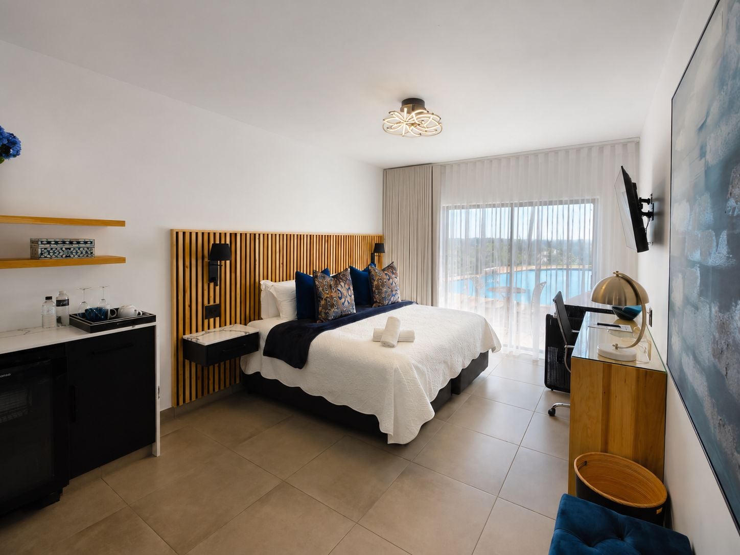 A modern hotel room with a bed, desk, and a view of a swimming pool.