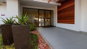 A modern building entrance with a glass door, a wooden slatted roof, and potted plants. - The Ridge Guesthouse (Richards Bay)