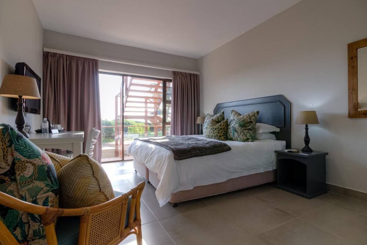 A hotel room with a bed, a chair, a desk, and a lamp.