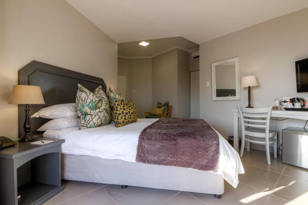 A hotel room with a bed, bedside table, lamp, chair, desk, and a mirror.