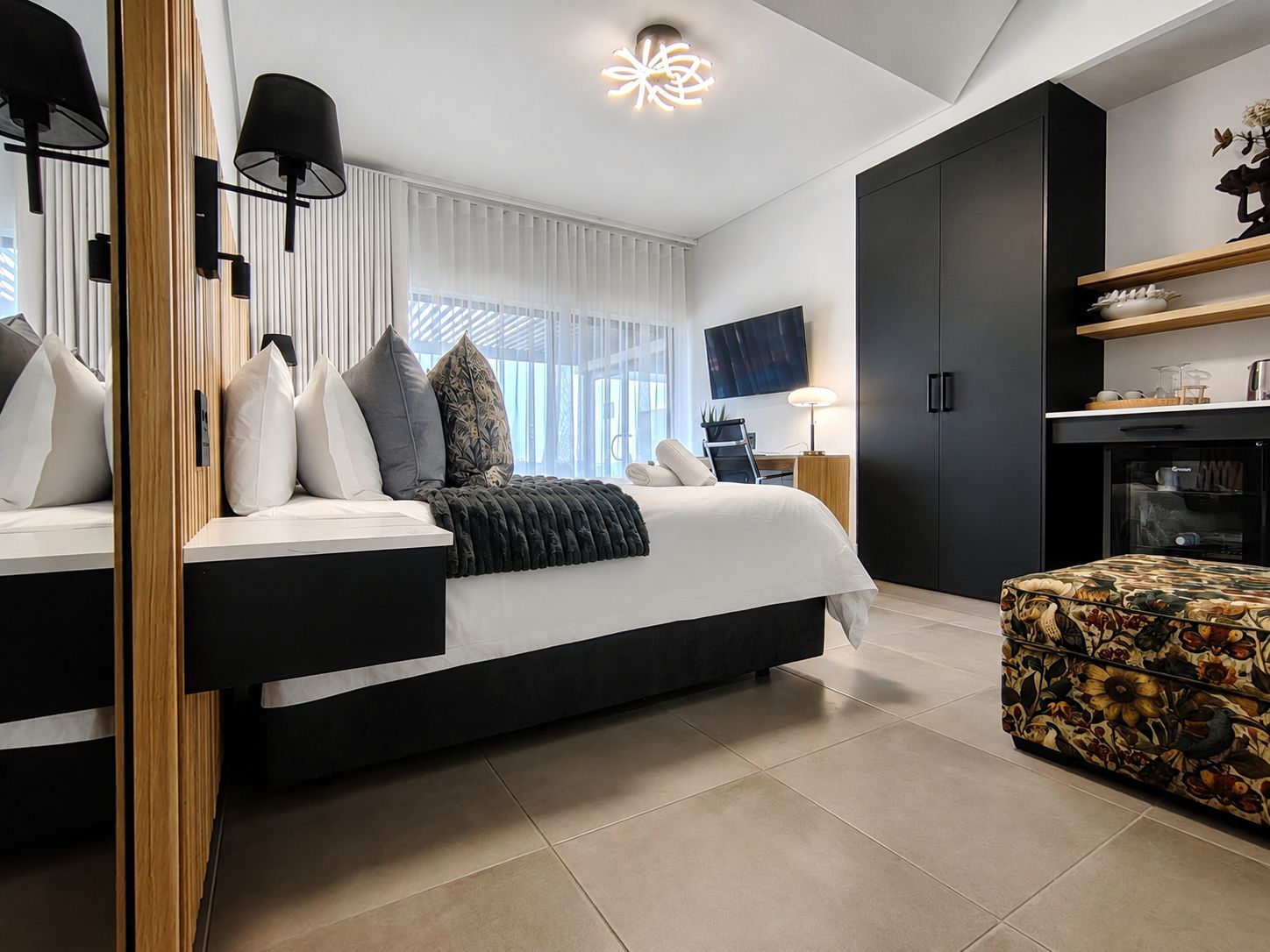 A modern bedroom with a large bed, bedside tables, a desk, and a television.