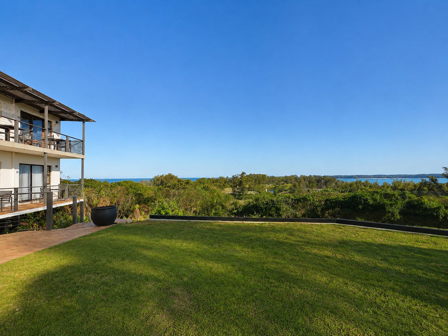 Un bâtiment moderne à deux étages, doté d’un balcon, d’une pelouse bien entretenue et offrant une vue sur l’océan.