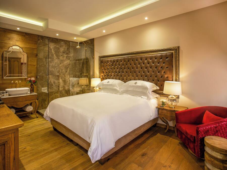 Una habitación de hotel con una cama grande, un escritorio de madera, una silla roja, un baño con espejo y una pared de mármol.