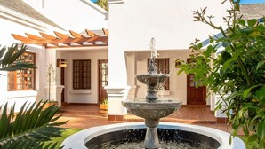 A white building with a fountain in the center, surrounded by greenery. - The Giglio Boutique Hotel (Germiston)