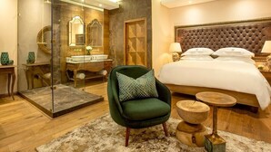 A modern hotel room with a large bed, a green armchair, a glass-enclosed shower, and a wooden floor. - The Giglio Boutique Hotel (Germiston)