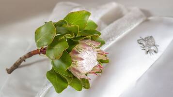 A white pillow with a decorative emblem and a green plant with pink flowers.