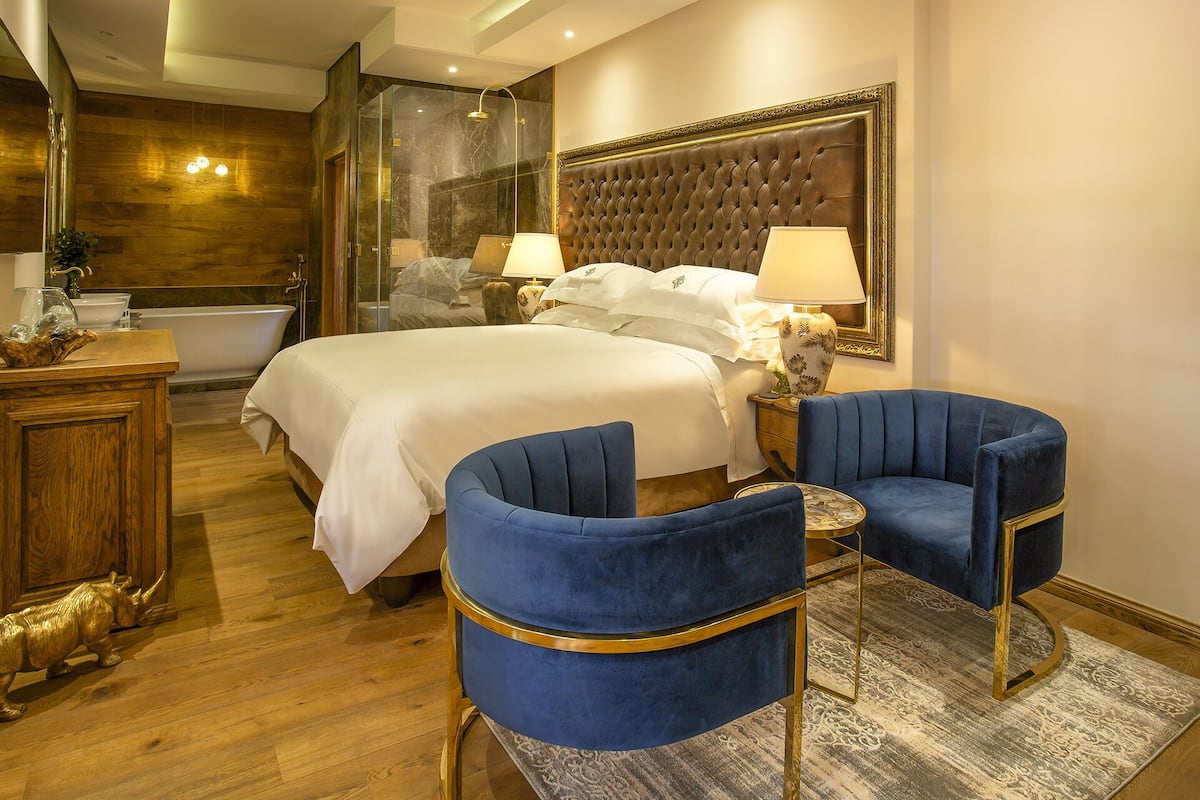 Ein Hotelzimmer mit einem großen Bett, zwei blauen Sesseln, einem runden Tisch, einem Spiegel und einer Badewanne.