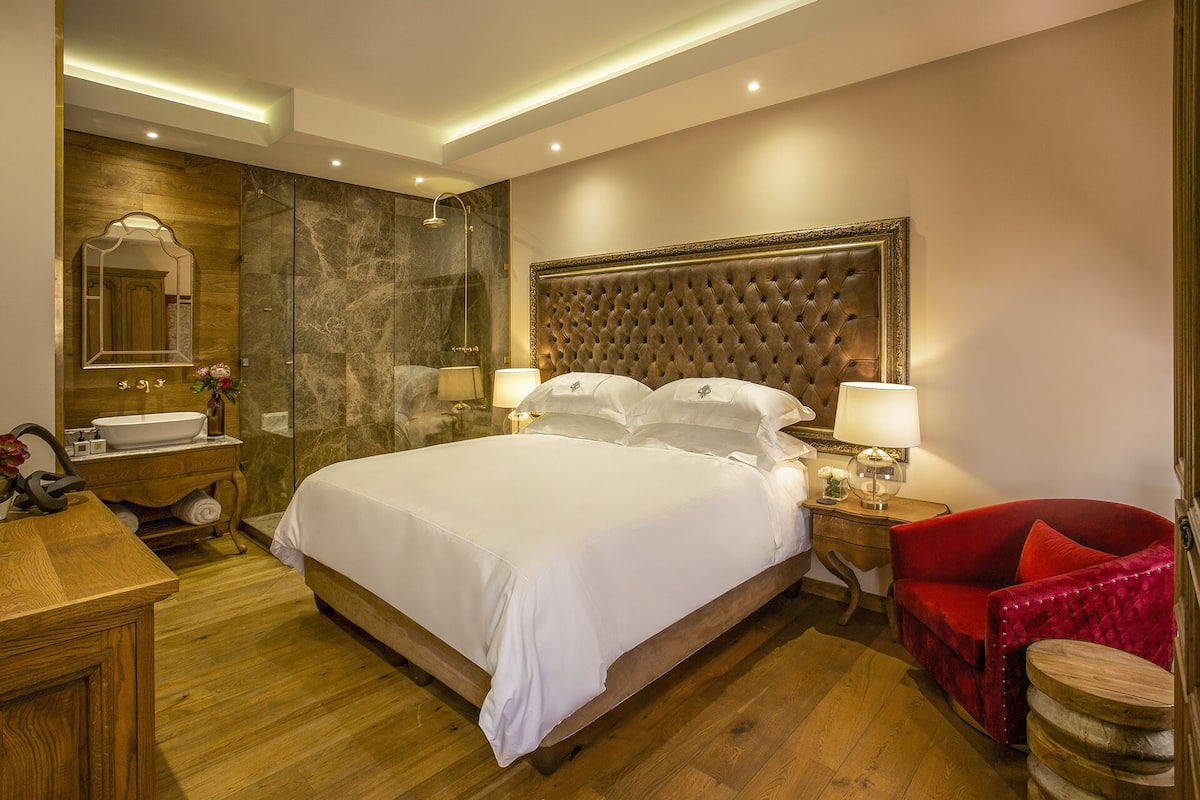 Ein Hotelzimmer mit einem großen Bett, einem hölzernen Schminktisch, einem roten Sessel und einer Marmorwand.