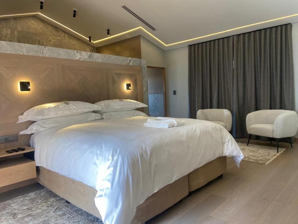 Ein modernes Schlafzimmer mit einem großen Bett, Nachttischen, einem Sessel und Blick ins Freie.