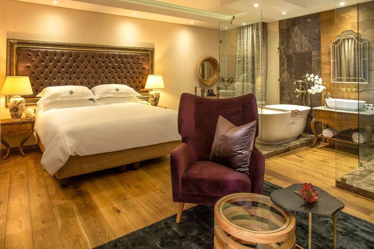 Ein Hotelzimmer mit einem großen Bett, einer Sitzecke mit einem Sessel, einer Badewanne und einer gläsernen Duschkabine.