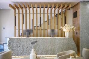 Balcão de atendimento com dois monitores, bancada de pedra e painel de ripas de madeira.