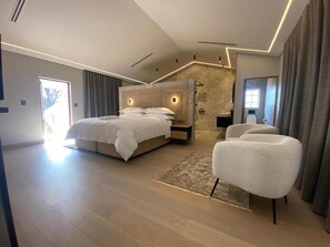 A modern bedroom with a large bed, a seating area, and a stone accent wall. - Zevenster Boutique Hotel (Germiston)