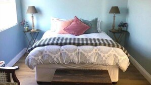 A bedroom with a bed, two bedside tables, a chandelier, and a window.