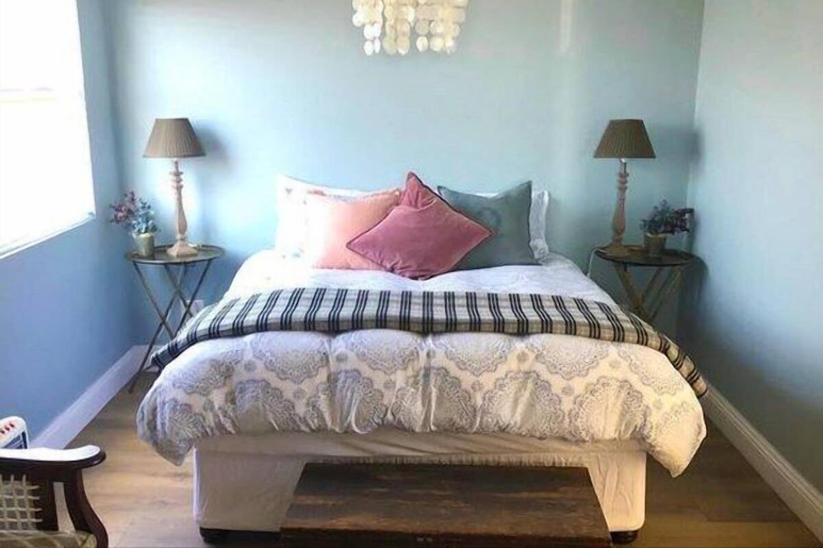A bedroom with a bed, two bedside tables, a chandelier, and a window.