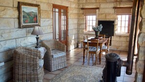 A cozy room with stone walls, wicker furniture, a fireplace, and a dining table.