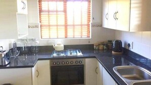 A compact kitchen with a gas stove, oven, and a window with blinds.