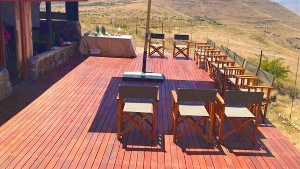 A wooden deck with outdoor seating and a table, overlooking a mountainous landscape.