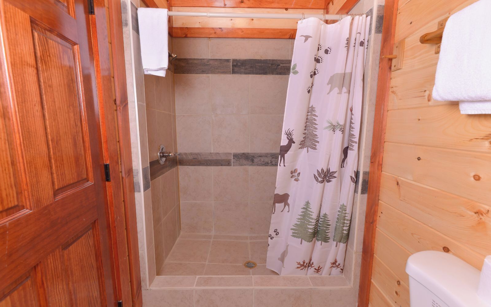 Un baño con paneles de madera, una zona de ducha, una puerta de madera y un inodoro blanco.