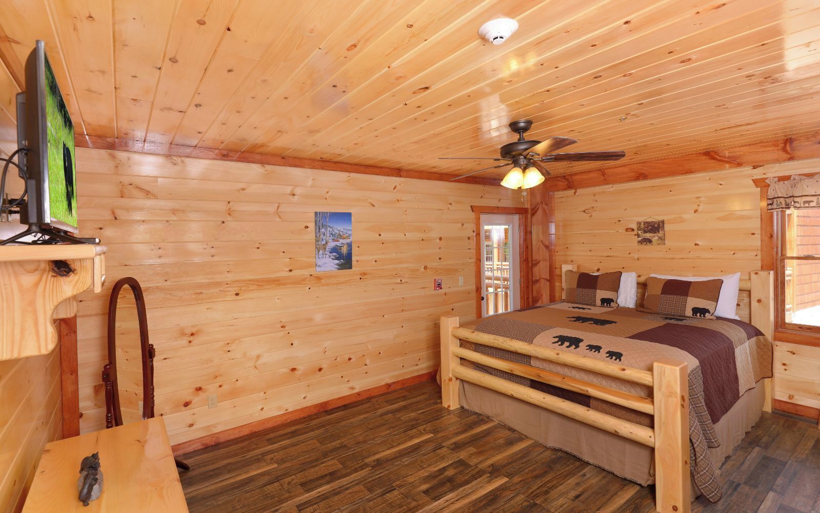 Une chambre dans un chalet en bois, avec un lit, un ventilateur de plafond, une télévision et un bureau en bois.