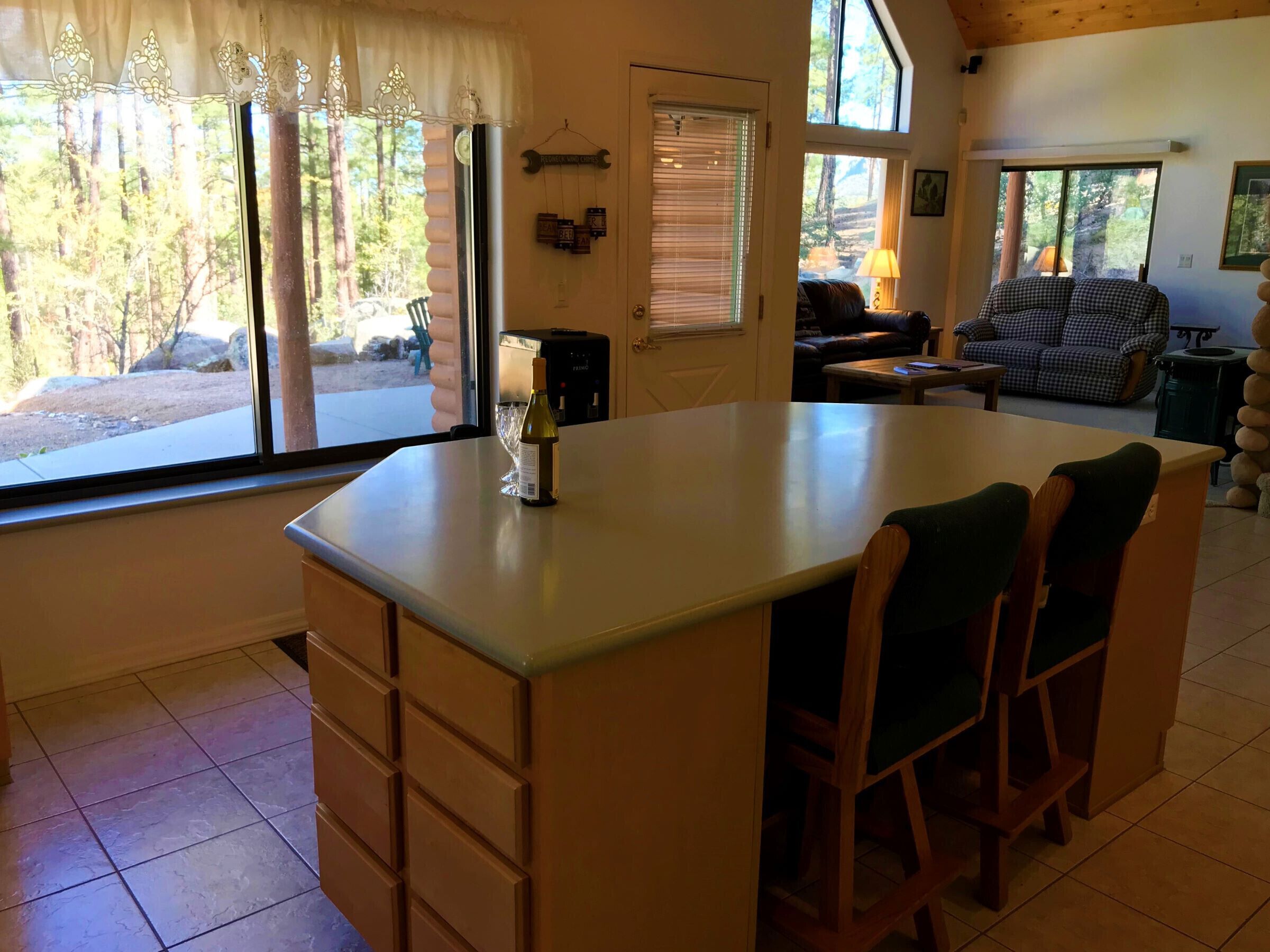 Una cocina acogedora con una isla grande, un comedor con un sofá a cuadros y vistas a un área boscosa a través de las ventanas.