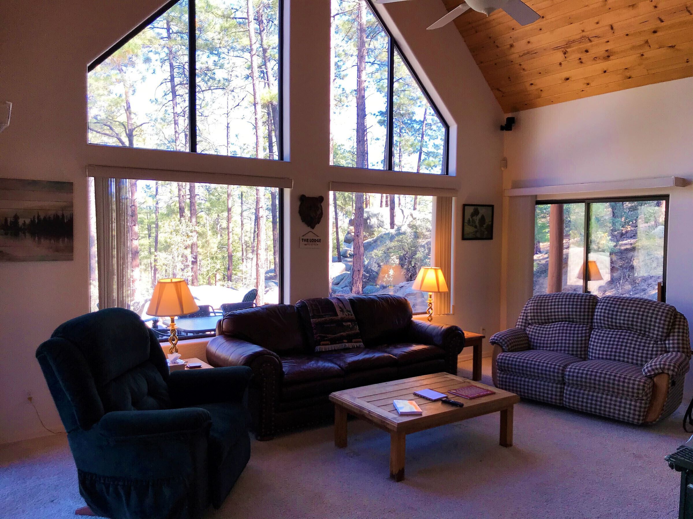A cozy living room with a large window, a wooden ceiling, and a fireplace.