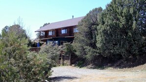 A two-story log cabin with a balcony, surrounded by dense trees and a gravel driveway. - Liberty Suite - Prescott Cabin Rentals (Prescott)