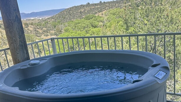Ett bubbelbad på ett trädäck med utsikt över ett kuperat landskap.