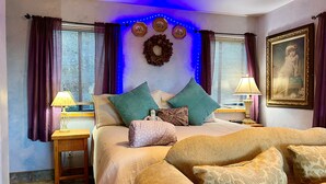 A bedroom with a bed, two bedside tables, a nightstand, a lamp, a framed picture, and a wall decoration.