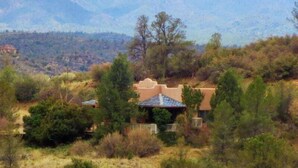 A house with a distinctive architectural style, surrounded by a natural landscape with mountains in the background.