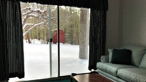 A room with a green carpet, a patterned sofa, a wooden coffee table, and a large window with curtains.