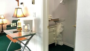 A room with a glass-top table, a coffee maker, a lamp, and a white dresser with a ruffled skirt.