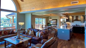 A spacious living area with a large sofa set, a dining table, and a kitchen area with a central island. - Longview Lodge - Prescott Cabin Rentals (Prescott)